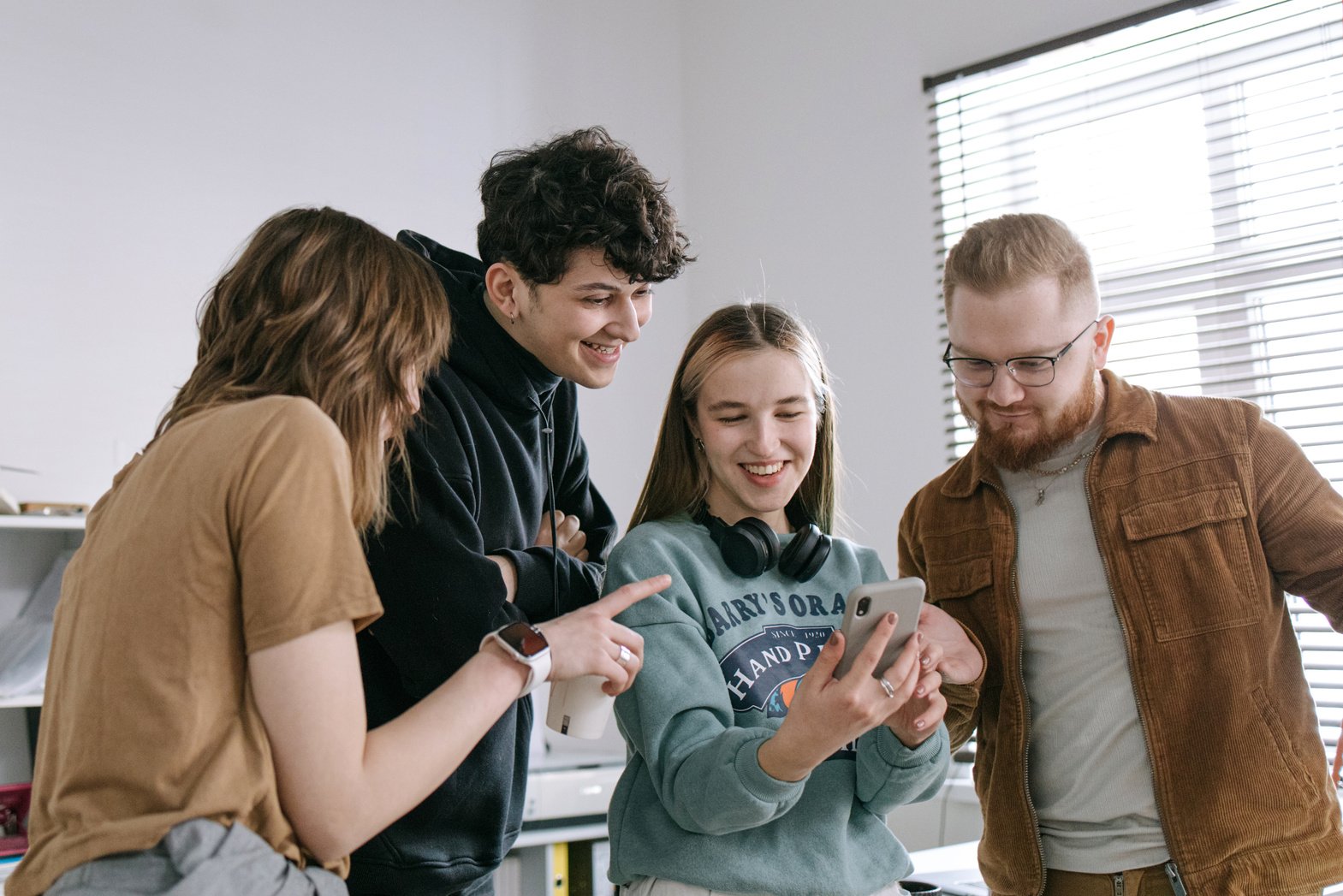 Group of People Smiling while Looking at Woman's Mobile Phone